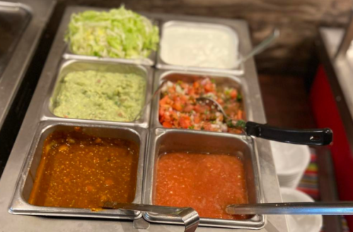 A metal serving tray with six compartments filled with lettuce, guacamole, sour cream, salsa, and two types of sauce.