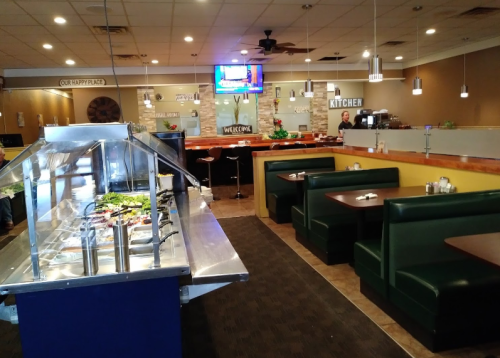 Interior of a restaurant featuring a buffet line, green booths, and a welcoming atmosphere with a TV in the background.
