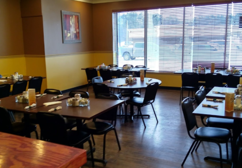 A spacious restaurant interior with empty tables, chairs, and large windows letting in natural light.