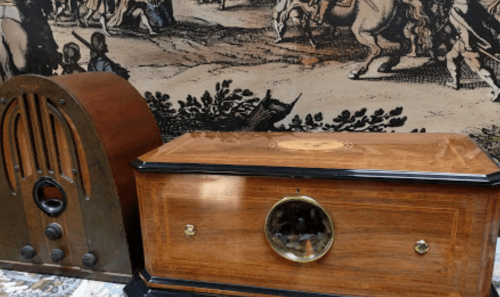 A vintage wooden radio and a decorative wooden box on a patterned backdrop featuring historical scenes.