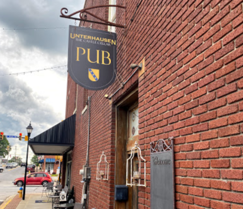 Sign for Unterhausen Pub hanging above a brick wall entrance, with a welcoming atmosphere and cloudy sky in the background.