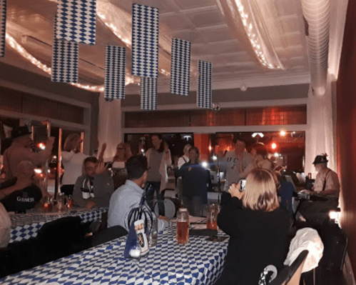 A lively restaurant scene with people socializing, blue and white decorations, and tables with drinks.