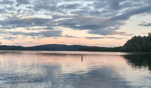 A serene lake at sunset, reflecting clouds and hills under a colorful sky.