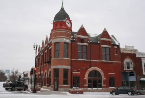 Historic red brick building with a clock tower, surrounded by snow, showcasing architectural details and a winter scene.