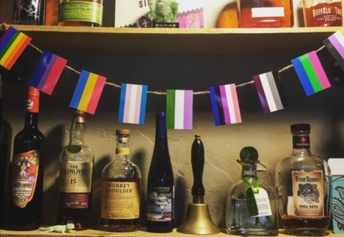 A shelf displaying various bottles of liquor, decorated with colorful pride flags.
