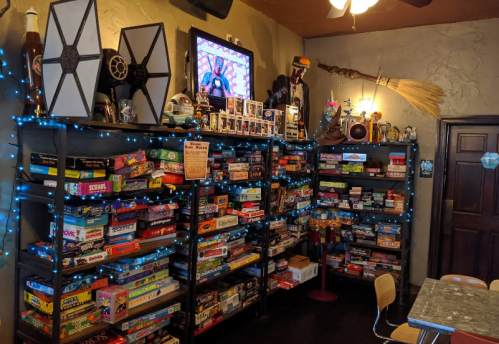 A cozy game room with shelves filled with board games, colorful lights, and a vintage TV displaying animated content.