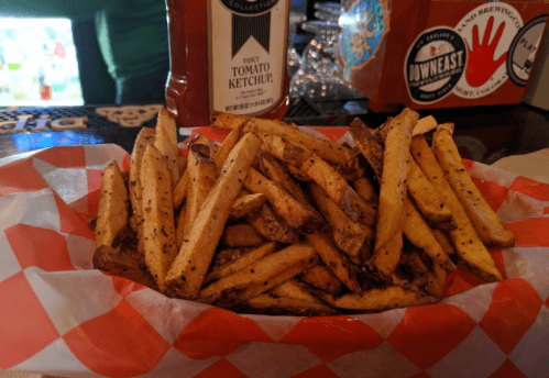 A basket of golden-brown French fries with a side of ketchup in a casual dining setting.