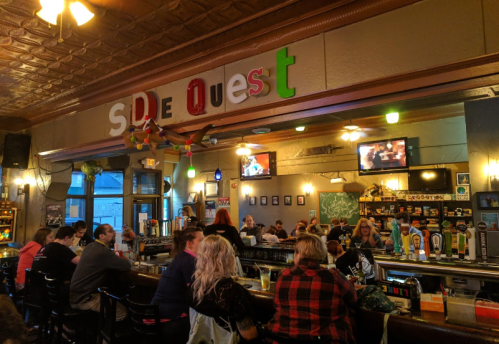 A lively bar scene with patrons seated at the counter, colorful decor, and a TV in the background.