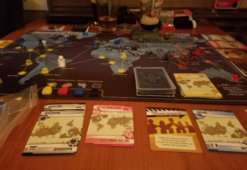 A tabletop game setup featuring a world map, player pieces, and cards labeled with city names and game instructions.