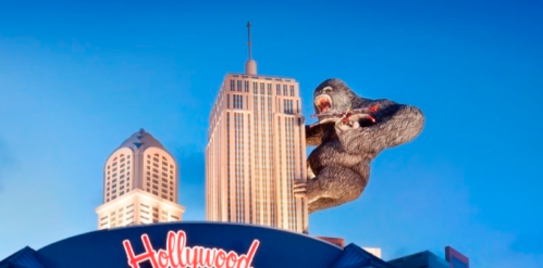 A giant gorilla clings to a skyscraper, with a Hollywood sign in the foreground against a blue sky.