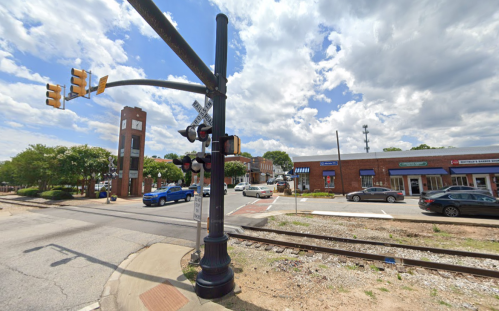 Traffic signal at a street intersection near a clock tower and shops, with a railroad crossing visible.