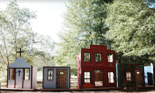 Colorful miniature buildings with various architectural styles set among trees in a sunny outdoor area.
