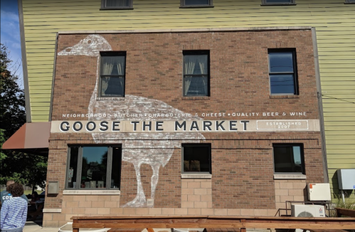 A brick building with a mural of a goose and the text "GOOSE THE MARKET" showcasing a butcher and cheese shop.