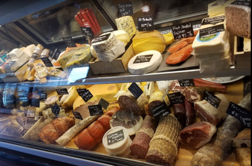 A display case filled with various cheeses and cured meats, each labeled with names and prices.