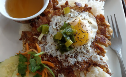 A plate of rice topped with a fried egg, crispy meat, green onions, and a side of salad and tea.