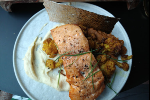 A plate featuring salmon, cauliflower, and a crispy garnish on a bed of creamy puree.