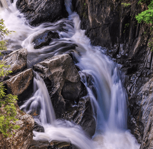 A cascading waterfall flows over dark rocks, surrounded by lush greenery.