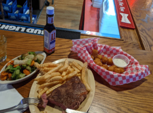 A plate with a steak, crinkle fries, a side of mixed vegetables, and a basket of tater tots with dipping sauce.