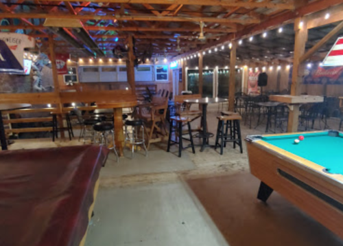 Interior of a rustic bar with pool table, wooden seating, and string lights, creating a cozy atmosphere.