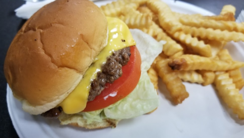 A cheeseburger with lettuce and tomato next to a serving of crinkle-cut fries on a white plate.