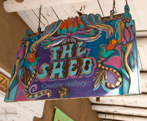 Colorful wooden sign reading "The Shed" with floral designs and the words "Creative Cookery" underneath.