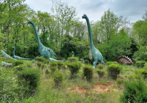 A group of large dinosaur sculptures among greenery, featuring long-necked dinosaurs and a stegosaurus in the background.