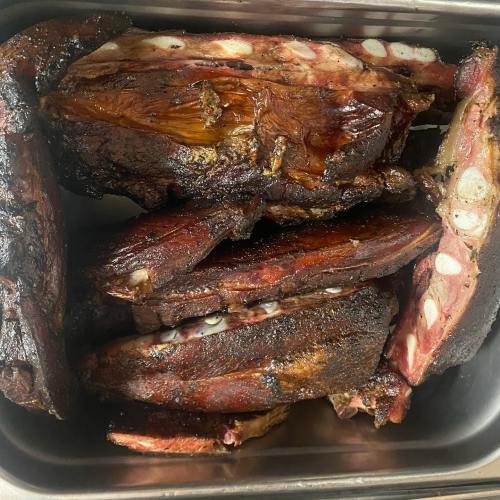 A close-up of smoked, charred meat ribs arranged in a metal container.