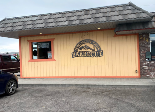Exterior of Smoky Gun Barbecue restaurant, featuring a yellow wall and a sign with the restaurant's name.