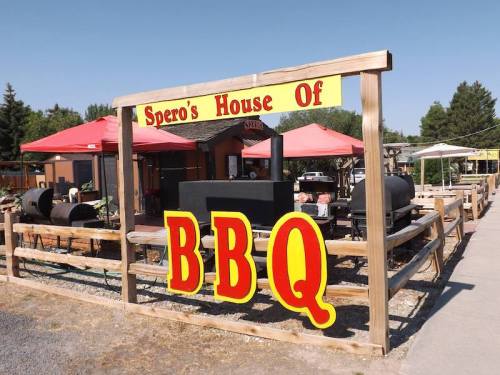 Sign for "Spero's House of BBQ" with outdoor cooking area and tents, set in a sunny location.