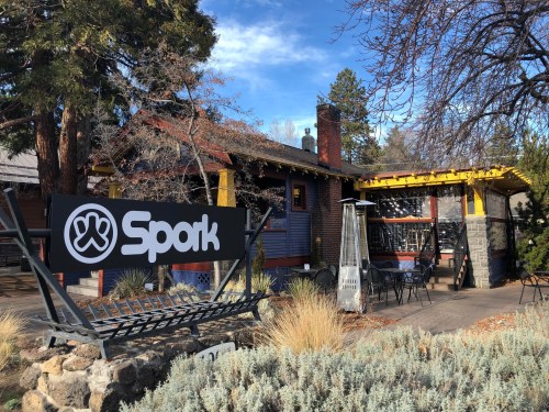 A cozy restaurant named "Spork" with outdoor seating, surrounded by trees and a clear blue sky.