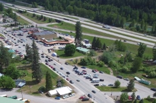 Aerial view of a busy intersection with cars, trees, and a restaurant near highways and green landscapes.