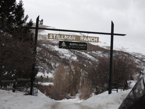 Sign for Stillman Ranch at the entrance, surrounded by snow-covered trees and mountains.