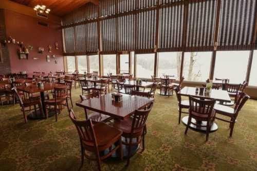 A spacious restaurant with wooden tables and chairs, large windows, and a cozy atmosphere overlooking a scenic view.