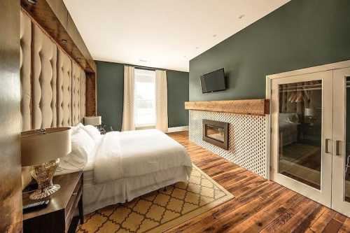 Modern bedroom with a large bed, stylish decor, a fireplace, and a TV on the wall, featuring wooden flooring.