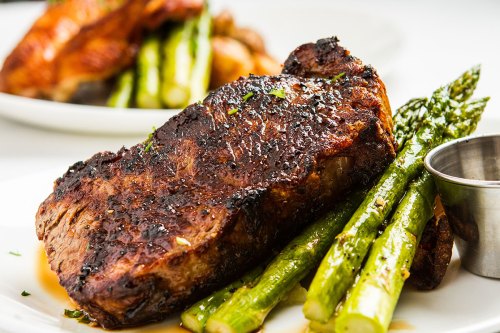 A juicy grilled steak served with asparagus on a white plate, garnished with herbs.