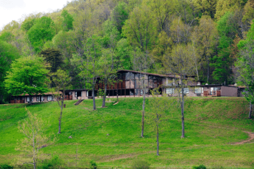 A modern building nestled on a green hillside, surrounded by trees and nature.