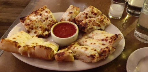 A plate of cheesy garlic bread with marinara sauce in a small bowl at the center.