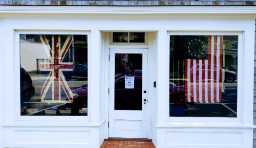 A storefront with large windows displaying a British flag and an American flag. The door is centered between the windows.