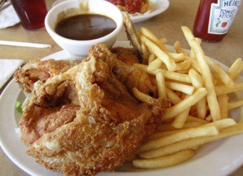 A plate of crispy fried chicken with French fries and a bowl of gravy on the side.
