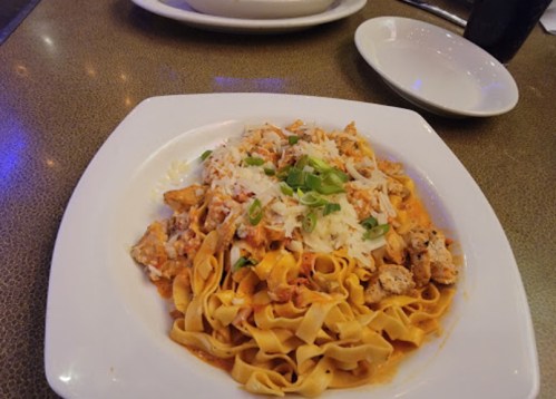 A plate of fettuccine pasta topped with chicken, cheese, and green onions in a creamy sauce.