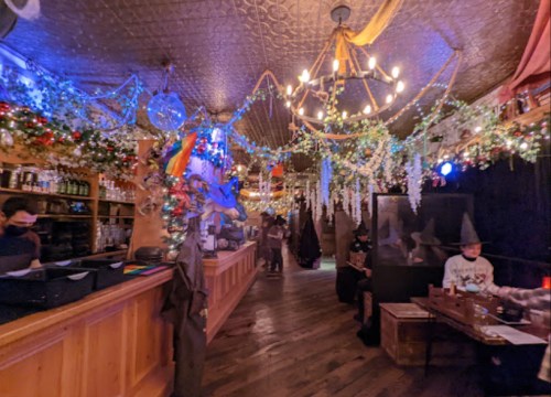A vibrant bar interior decorated with colorful lights, greenery, and festive ornaments, featuring patrons enjoying the atmosphere.
