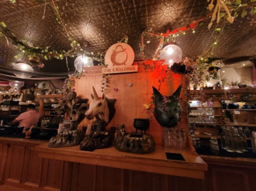 A whimsical bar with animal head mounts, including a unicorn, surrounded by plants and warm lighting.