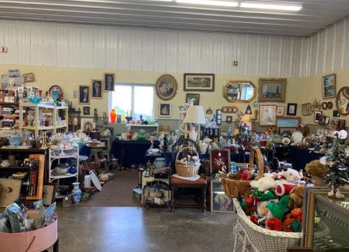 A cluttered antique shop filled with various collectibles, furniture, and decorations, including framed pictures and holiday items.