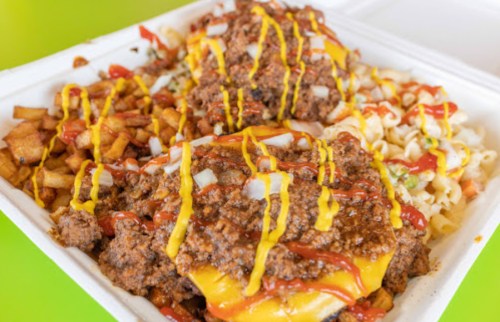 A takeout container filled with two cheeseburgers topped with chili, onions, ketchup, and mustard, alongside fries and pasta.