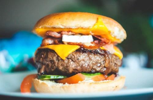 A close-up of a juicy burger with cheese, bacon, lettuce, and tomato on a toasted bun.