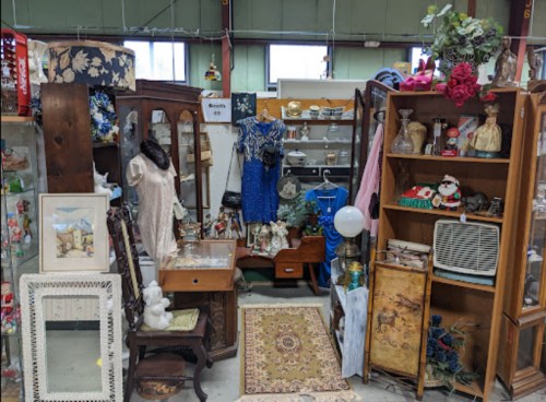 A cluttered antique shop display featuring vintage clothing, furniture, and decorative items.