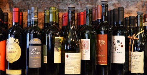 A variety of wine bottles displayed on a shelf, featuring different labels and colors against a rustic background.