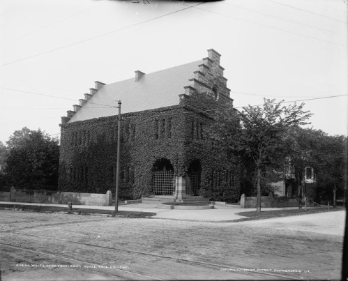 Historic ivy-covered building with a large entrance, surrounded by trees and a gravel path. Black and white photo.
