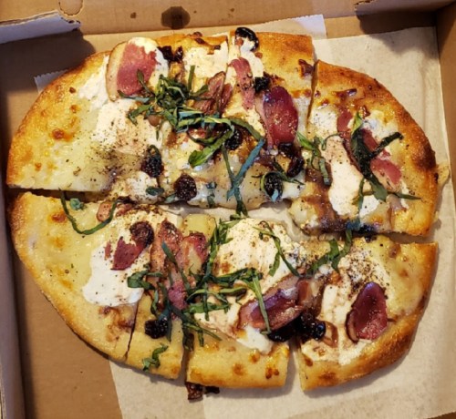 A sliced flatbread pizza topped with chicken, bacon, herbs, and drizzled with sauce, served in a pizza box.