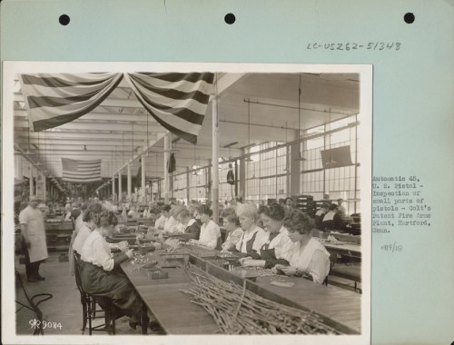 Women working at a factory assembly line, assembling products, with American flags hanging in the background.